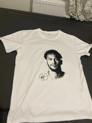 Vit t-shirt med porträtttryck - Vit t-shirt med svartvitt porträtttryck och signatur på framsidan. Klassisk rund hals och korta ärmar. T-shirten är i mjukt material och har en clean look utan tryck på baksidan. Perfekt för dig som gillar grafiska motiv.