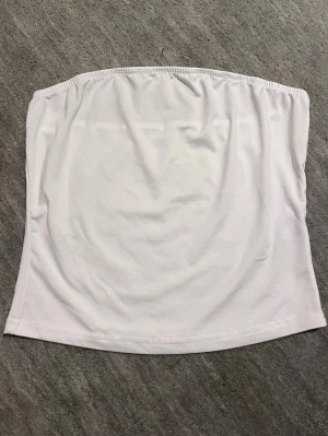 Vit bandeau topp - Vit bandeau topp med resår längs överkanten som inte syns när man har på sig den men som göra att den sitter på bra. Bandeau toppen är använd endast en gång så den är i ett väldigt fint skick. 