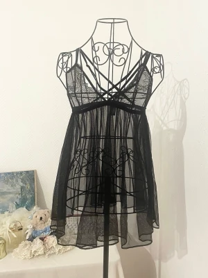 Svart transparent spetsklänning från Victoria's Secret - En svart kortklänning i transparent mesh med spetsdetaljer och tunna axelband från Victoria's Secret. Storlek: M, passar 36-38. Dockans storlek: 34.