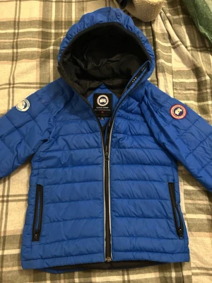 Canada Goose dunjacka - Säljer en blå dunjacka från Canada Goose med huva och coola patchar på ärmarna. Jackan har svarta dragkedjor och är quiltad för extra värme. Perfekt för dig som vill ha en snygg och funktionell jacka när det är kallt ute. Nypris: 5000 Jag har inte kvittot, vilket förklarar de lägre priset.