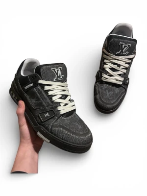 Louis Vuitton svarta sneakers denim - Louis Vuitton sneakers i svart denim med vita snören och tydliga LV-loggor på plösen och sidan. Snygga kontrastsömmar och detaljer i svart och vitt. Tillverkade i Italien, insida i vitt tyg och platt sula. Perfekt för dig som gillar exklusiva streetwear-vibes. Använda 3 ggr, ingen box har kvitt.