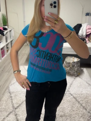 Blå SOC t-shirt med tryck - Blå t-shirt från SOC med stort tryck i svart och lila på framsidan. Klassisk rund halsringning och korta ärmar. Skön och lätt i bomull, perfekt till chill dagar eller när du vill ha en sportig vibe.