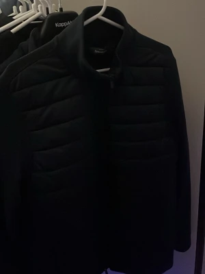 Mörkblå cardiganfrån Dressmann - Säljer en mörkblå cardigan från Dressmann i storlek M. Cardiganen har en stilren design med horisontella quiltade partier och dragkedja framtill. Perfekt för dig som vill ha en enkel och snygg cardigan med modern känsla.