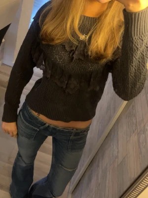 Mörkgrå stickad tröja med spets  - Säljer en mörkgrå stickad tröja från Lindex med snygga spetsdetaljer och volanger framtill. Tröjan har långärmade ribbade muddar och ett coolt mönster i stickningen💞