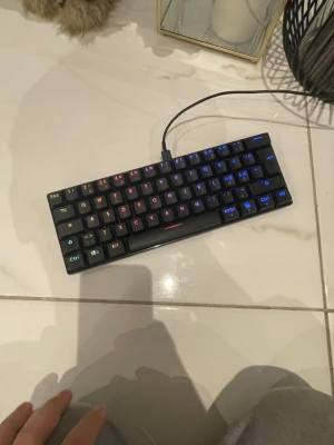 Deltaco Gaming 60% Mekaniskt Tangentbord - Kompakt 60% mekaniskt tangentbord från Deltaco Gaming med RGB-belysning. Perfekt för gaming och skrivbord med begränsat utrymme. Tangenterna ser fräscha ut och tangentbordet är i gott skick utan synligt slitage eller defekter. USB-anslutning för enkel installation.