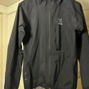 Svart Haglöfs Gore-Tex vindjacka - Haglöfs L.I.M Critus Jacket är en lätt och smidig jacka som lämpar sig för aktiv vandring, och den passar även för vardagsbruk under regniga dagar. Jackan tar lite utrymme när den är nedpackad, vilket är guld värt under dagar när vädret är skiftande. Lätt, minimalistisk skaljacka i vattentätt, vindtätt och ventilerande Gore-Tex Paclite-material (28 000 mm vattenpelare).  Köpt för ca 3 år sen men i väldigt bra skick, inga skavanker. Köpt för 2199 kr.