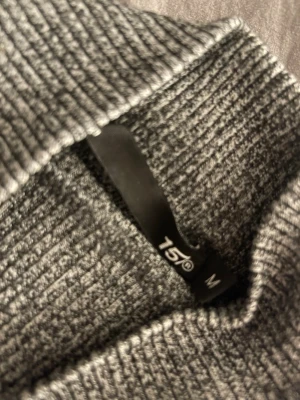 Grå ribbad polotröja från 157 - Säljer en grå ribbad polotröja från 157 i storlek M. Tröjan har lång ärm och en hög krage som ger en snygg och chill look. Materialet är mjukt och stretchigt, perfekt för lager-på-lager under hösten och vintern. Passformen är normal och den är enkel att matcha.