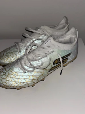 Fotbollsskor - Säljer ett par Skechers SKX_01 1.5 FG i storlek 42,5, innermått 27 cm. Skorna är avsedda för FG (Firm Ground-naturgräs) men har även använts på konstgräs. Använda totalt 4 träningar: 2 på konstgräs och	2 på naturgräs  Skorna är i mycket fint skick med normalt lätt slitage, se bilder. Inga skador eller sprickor, bra grepp i dobbarna.  Anledningen till försäljning är helt enkelt att de inte passade min fotform optimalt. Snygg vit design med gulddetaljer. Öppen för bud!☺️