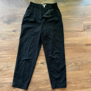 Svarta kostymbyxor  - Svarta kostymbyxor från H&M med klassisk rak passform och pressveck. Byxorna har hällor i midjan och stängs med dragkedja och knapp. Perfekta för en stilren look och enkla att matcha med olika överdelar.