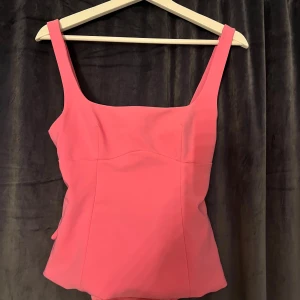 Rosa linnetopp med rosett från Zara - Supersnygg rosa linnetopp från Zara med breda axelband och fyrkantig ringning. Baksidan har en stor rosett och en öppen detalj som ger en unik look. Perfekt för dig som vill sticka ut med en färgglad och trendig topp.💓