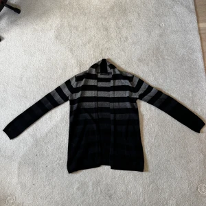 Randig kofta från Stockh LM, svart/grå - Snygg lång kofta från Stockh LM i svart och grått med breda horisontella ränder. Koftan har öppen front, två fickor fram och långa ärmar. Perfekt för lager-på-lager och chill vibes. Mjuk och skön stickad känsla. Storlek S.