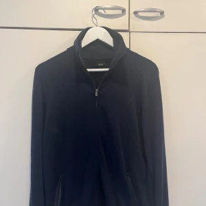Mörkblå stickad tröja Massimo Dutti - Mörkblå stickad tröja från Massimo Dutti med zip och hög krage. Tröjan är i mjuk ull och har lång ärm, perfekt för kyligare dagar. Enkel och stilren design som funkar till det mesta.