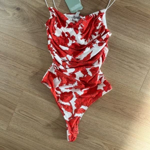 Vit och röd blommig body oanvänd  - Supersnygg body.med blommigt mönster. Sitter tight och har smala axelband.