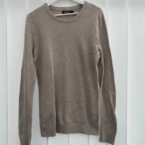 Beige stickad tröja från Dressmann - Säljer en stilren beige stickad tröja från Dressmann i storlek M. Tröjan har rund halsringning, ribbade muddar och är långärmad. Perfekt för lager-på-lager och enkel att matcha med jeans eller chinos.