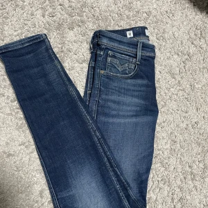 Replay Anbass blå jeans herr - Snygga Replay Anbass jeans i st W28 L32, kan gå ner i pris vid snabb affär. klassisk blå tvätt med diskreta slitningar och kontrastsömmar. Modellen har fem fickor, smal passform och läderpatch bak i midjan. Perfekta för dig som gillar en modern och stilren look. Materialet är mjukt och stretchigt jeans.