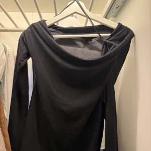 Svart långärmad tröja med drapering - Svart långärmad klänning med snygg draperad halsringning och asymmetrisk axeldetalj. Klänningen har en elegant och enkel design som ger en stilren look. Perfekt för dig som gillar minimalistiska plagg med en twist. Från Nelly