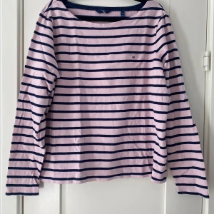 Rosa och marinblå randig tröja GANT - Säljer en rosa långärmad tröja från GANT med marinblå horisontella ränder och rund hals. Tröjan har ett litet broderat GANT-emblem på bröstet och är gjord i mjuk bomull. Perfekt för dig som gillar klassisk och chill stil. Mått Över bröstet: ca 58 cm Längd från axeln och ner: ca 60 cm  100% bomull  Kommer från ett djur och rökfritt hem.