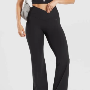 Flare byxor från Gymshark - Snygga svarta träningsbyxor från Gymshark med hög midja och V-formad linning. Byxorna har ett wide fit och är tillverkade i mjukt, stretchigt syntetmaterial som sitter bekvämt. Perfekta för gymmet eller chill. Diskret logga på höften.
