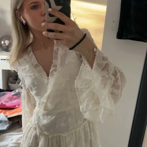 Vit volangklänning från Boohoo Petite - Supersöt vit klänning från Boohoo Petite med volanger och v-ringning. Klänningen har långa,  ärmar och ett  blommigt mönster i tyget. Perfekt för studenten!