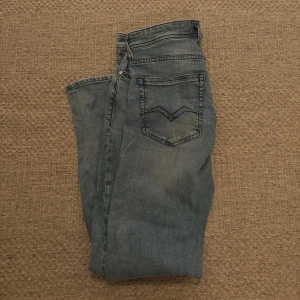 Replay Grover ljusblå jeans straight fit - Säljer ett par Replay Grover jeans i ljusblå tvätt med raka ben och klassisk femficksdesign. Jeansen har snygga slitningar, knäppning med knappar och diskret Replay-logga vid fickan. Perfekta för dig som gillar en clean och avslappnad look.