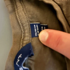 Olivgrön tröja från Gant med brodyr - Olivgrön tröja från Gant med rund halsringning och broderad Gant-logga samt sköld på bröstet. Tillverkad i mjuk bomull, perfekt för en avslappnad och stilren look. Passar folk mellan 155-165 cm