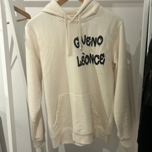 Giveno Léonce hoodie - Säljer en beige hoodie från Giveno Léonce med svart tryck framtill. Tröjan har huva med snörning, känguruficka och långa ärmar. Perfekt för dig som gillar en clean och chill stil. Storlek M, bra skick. Nypris 1500