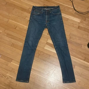Blå skinny jeans från Nudie Jeans - Snygga blå jeans från Nudie Jeans i modellen skinny. Jeansen har en mörk tvätt och detaljerade broderier på bakfickorna samt läderpatch med logga i midjan. Perfekt passform för dig som gillar smal siluett.