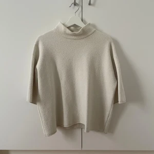 Vit tröja med trekvartsärm - Vit tröja med trekvartsärm. Tröjan har en mjuk och lite grov textur, hög krage och avslappnad passform. 