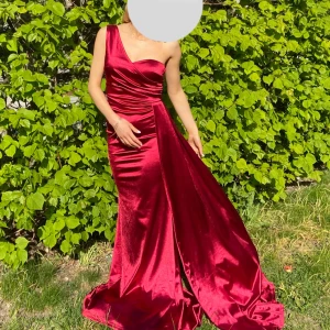 Vinröd lång klänning i sammet - Säljer en vinröd långklänning i glansig sammet med oneshoulder och figurnära passform. Klänningen har draperade detaljer och en elegant slits framtill. Klänningar är i storlek S men passar perfekt en xxs/xs. 