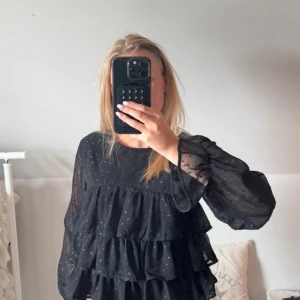 Svart volangblus med glitterprickar - Säljer en svart blus med flera lager volanger och små diskreta prickar av typ glitter/paljett. Blusen har transparenta, långärmade ärmar och en luftig passform. Perfekt för dig som gillar en trendig och lekfull stil med extra volym och detaljer. I storlek 158/164 men passar mig som har xs/xxs. 🫰🏻