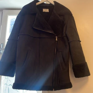 Svart teddyjacka från Karo Kauer - Säljer en svart teddyjacka från Karo Kauer med bred krage och mysigt foder. Jackan har grov dragkedja, uppvikta ärmslut och två fickor framtill. Oversized passform och coola sömdetaljer ger en modern vibe. Perfekt för kalla dagar när du vill vara både varm och snygg.