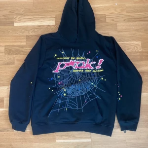 Svart hoodie från SP5DER med tryck - Cool svart hoodie från SP5DER i bomull med färgglatt spindelnäts- och stjärntryck på ryggen samt texten 'nevermind the spider, heres the slime'. Klassisk huva och ribbade muddar. Perfekt för dig som vill sticka ut med streetstyle.