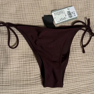 Mörkbrun bikiniunderdel - Snygg mörkbrun bikiniunderdel från H&M med knyt i sidorna och rynkad detalj bak. Helt ny