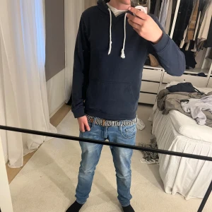 Mörkblå hoodie med vita snören - Säljer en stilren mörkblå hoodie med vita dragsnören och känguruficka framtill. Tröjan har en klassisk passform och är perfekt för chill dagar. Materialet känns mjukt och skönt mot huden. Passar dig som gillar enkel och clean streetstil. Jag är 184 och 72 kg, tröjan är av märket ”pier one” och i storlek S. Hör av dig om du har frågor eller vill diskutera pris.👍