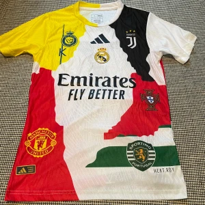 Cristiano Ronaldo collage fotbollströja - Unik kortärmad fotbollströja från Adidas med collage av klubbmärken: Real Madrid, Juventus, Manchester United, Sporting Lissabon och Portugals landslag. Färgstark design i vitt, rött, gult, svart och grönt. Tryck med 'Ronaldo 7' på ryggen. Tillverkad i lätt funktionsmaterial.