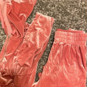 Rosa set från Fashion Nova - Mjuk och glansig rosa set i velour från Fashion Nova. Tröjan har huva, dragkedja framtill och långa ärmar med breda muddar. Perfekt för chill dagar eller när du vill vara extra comfy. Matchande byxor ingår