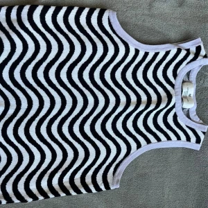 Svartvit vågig linnetopp från H&M - Säljer en snygg ärmlös linnetopp från H&M med svartvitt vågigt mönster. Toppen har rund halsringning och är tillverkad i mjuk bomull, perfekt för en cool och trendig look.