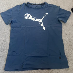 Blå Puma t-shirt med logga - Snygg blå t-shirt från Puma med stor vit logga framtill. Klassisk passform och rund halsringning. Tillverkad i mjuk bomull som är skön att ha på sig. 