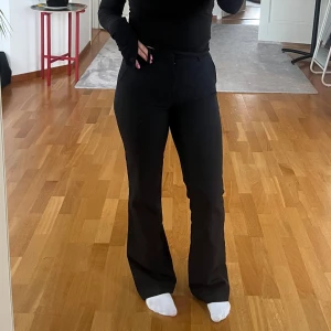 Svarta bootcut kostymbyxor - Snygga svarta bootcut byxor med hög midja och klassisk passform. Byxorna har en stilren look och är perfekta för dig som gillar en tidlös och trendig siluett. Materialet känns mjukt och följsamt mot kroppen.