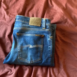 Blå Nudie Jeans, storlek 31/34 - Säljer ett par klassiska blå jeans från Nudie Jeans med snygga kontrastsömmar och vågmönster på bakfickorna. Modellen har slim passform och storleken w31 L34