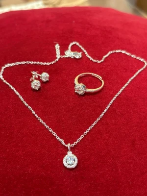 Snygg äkta silver smyckeset m S 925 🩶 - Set med halsband, örhängen och ring i silverfärg med gnistrande stenar. Halsbandet har ett runt hänge med små stenar runt en större mittsten. Örhängena matchar med samma design och ringen har en liknande steninfattning. Perfekt för dig som gillar bling och stilrena detaljer.