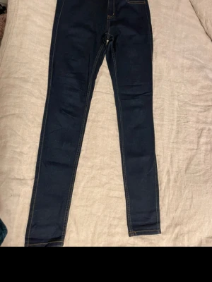 Mörkblå jeans från Pieces - Snygga mörkblå skinny jeans från Pieces med klassisk femficksdesign och kontrastsömmar i orange. Jeansen har hög midja och är gjorda i stretchigt bomullsmaterial för en tight passform. Perfekta för dig som gillar en stilren och enkel look.