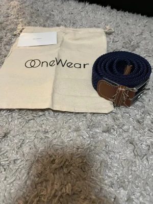 Marinblå flätad OneWear bälte - Säljer mitt OneWear bälte. Flätat bälte. Det är använt ganska mycket men har lite kvar i sig. Tygpåse och tack kort kommer med vid köp🤗skriv vid funderingar osv.