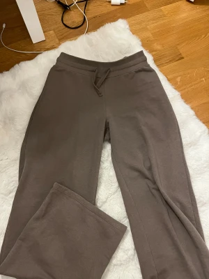 Bruna mjukisbyxor från Gina Tricot - Säljer ett par bruna mjukisbyxor från Gina Tricot i storlek M. Byxorna har ribbad midja med snörning och raka ben. Sköna och avslappnade, perfekta för chill dagar. Materialet är mjukt och känns bekvämt mot huden.