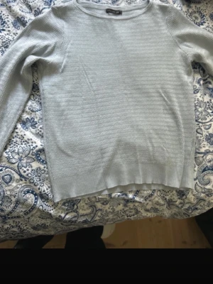 Ljusgrå stickad tröja från Stockh LM - Snygg ljusblå stickad tröja från Stockh LM i storlek S. Tröjan har ett diskret zigzag-mönster och rund hals. Långärmad och med ribbade muddar vid ärmslut och nederkant. Perfekt för dig som gillar stilrena och enkla plagg.
