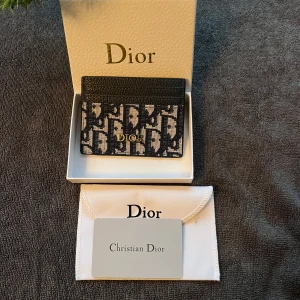 Plånbok - Säljer en snygg plånbok med klassiskt monogrammönster i svart och beige. Plånboken har guldfärgad -logga framtill och är tillverkad i en mix av skinn och textil. Perfekt för kort och smågrejer, levereras med originalask och dustbag.