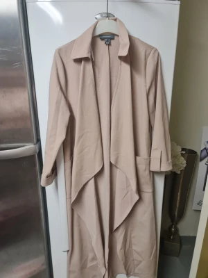 Beige trenchcoat från Atmosphere - Säljer en beige trenchcoat från Atmosphere i storlek 36. Jackan har en snygg omlott-design med bred krage, långa ärmar och stora fickor framtill. Materialet är mjukt och har en lätt struktur, perfekt för dig som gillar stilrena och enkla plagg.
