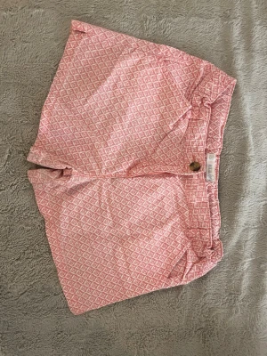 Rosa mönstrade shorts  - Säljer ett par rosa shorts köpta i Spanien med vitt blommigt mönster. Storleken motsvarar en XS-s