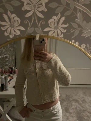 Beige stickad kofta med pärlknappar - Säljer en beige stickad kofta med croppad passform och långa ärmar. Koftan har dekorativa guldknappar framtill och två bröstfickor med knapp. Aldrig använd!