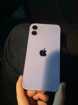 iPhone 12 - Snygg lila iPhone 12 med dubbla kameror och modern design. Skärmen har några synliga repor och mindre slitage på kanterna, men mobilen fungerar som den ska. Perfekt för dig som vill ha en pålitlig och stilren smartphone till ett bra pris.
